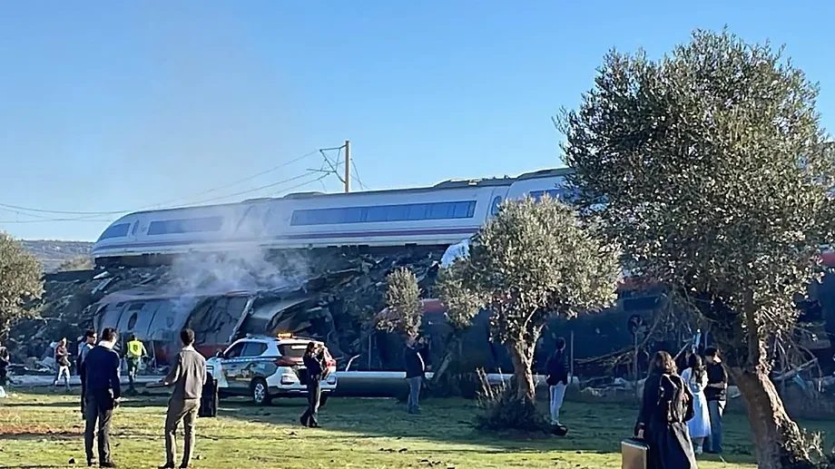 Un vagón del AVE queda sobre los restos del tren tras el choque, junto a un vehículo de emergencias y varias personas en un campo de olivos
