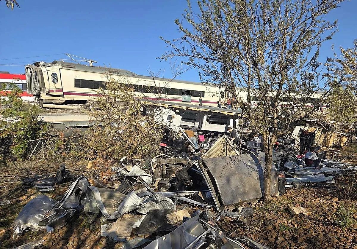 Restos metálicos del tren esparcidos junto a la vía, con un vagón del AVE dañado al fondo
