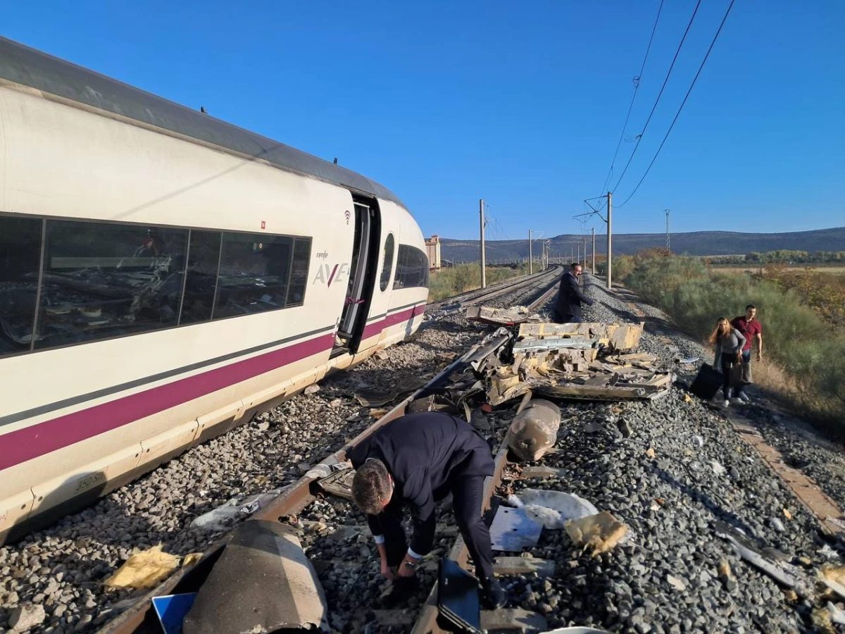 Un vagón del AVE inclinado sobre la vía, con restos del choque y pasajeros caminando entre las vías