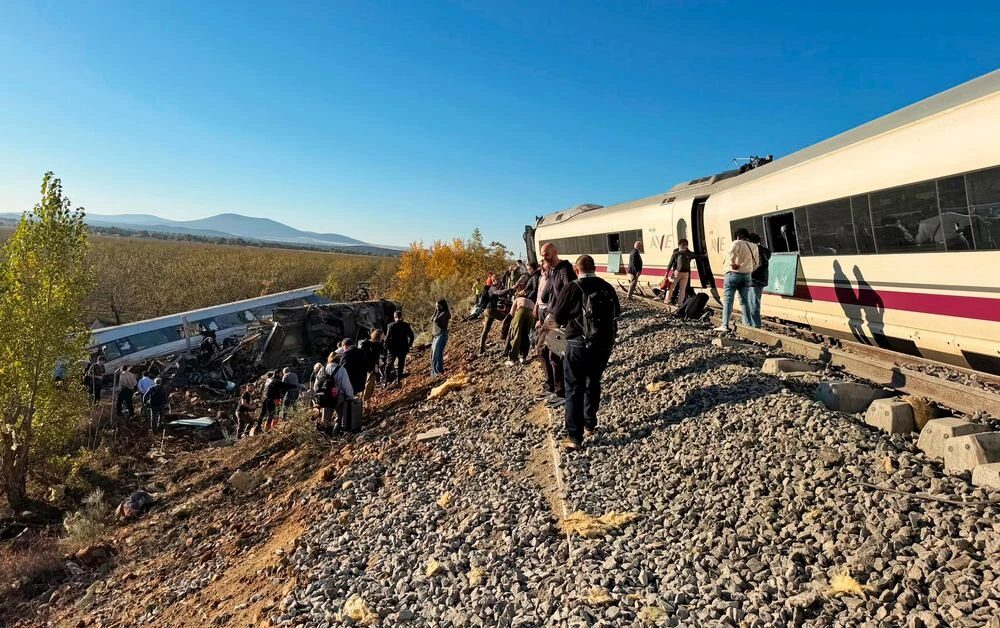 Pasajeros caminan junto a la vía tras el accidente, con un vagón destrozado al fondo del terraplén