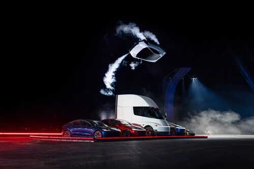 El Roadster en el aire, girando sobre sí mismo y dejando estelas de humo blanco, por encima de una fila de vehículos de Tesla con un camión Semi en el centro.